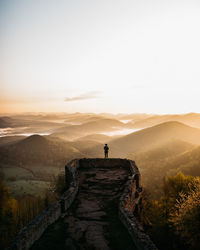 Rear view of man standing on a castle ruin in the mountains against sky