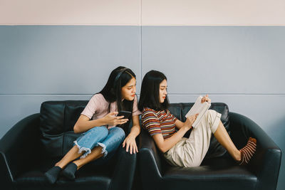 Young woman using phone while sitting on sofa against wall