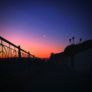 Silhouette birds on bridge against sky at sunset