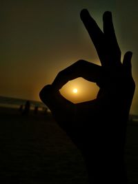 Silhouette person holding sun against sky during sunset