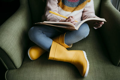 Girl writing in book while sitting on chair at home