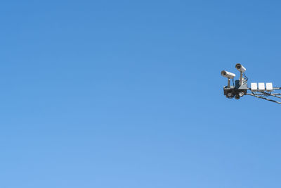 Low angle view of security camera against clear blue sky