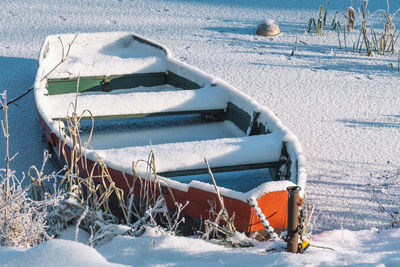 Wooden colorful boat stacked on a frozen lake covered by snow on the beach with reeds