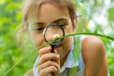 Front view of girl looking at snail on grass through magnifying glass