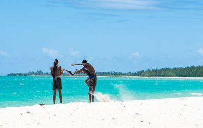 Friends playing on the beach against sky