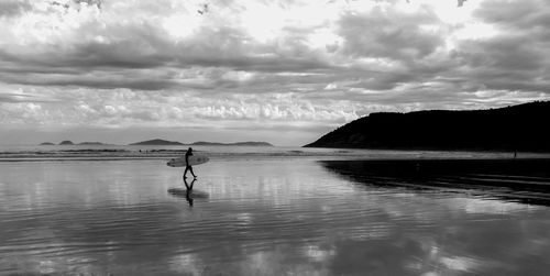 Person with surfboard walking at beach against sky