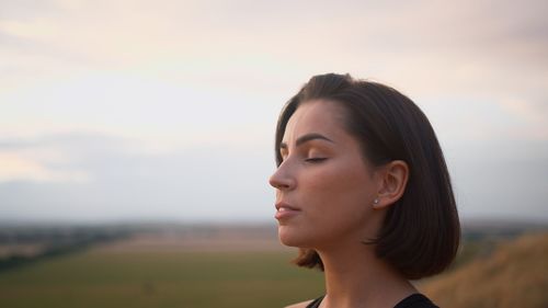Close-up of young woman looking away against sky during sunset