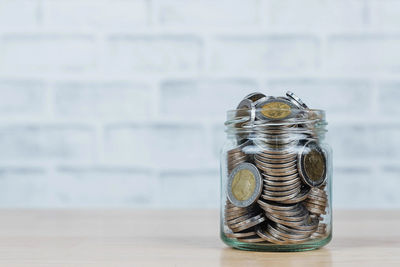 Close-up of coins in jar on table against wall