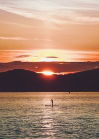 Silhouette person in sea against sky during sunset