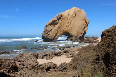 Rock formation at sea shore against clear blue sky