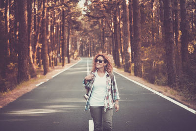 Smiling woman walking on road amidst forest