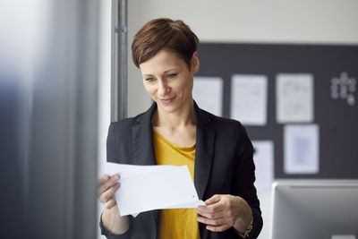 Attractive businesswoman standing in office, readiing document