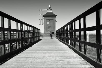 Man walking on footbridge by building against sky