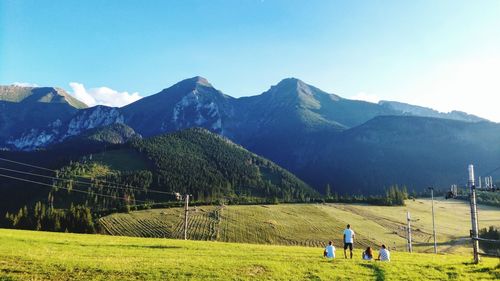 People on field by mountains against clear sky