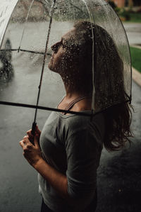 Rear view of woman with umbrella standing in rain