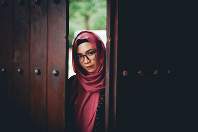 Portrait of young woman standing against door