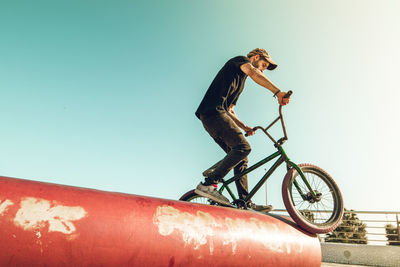 Man riding bicycle on red metallic pipe against sky