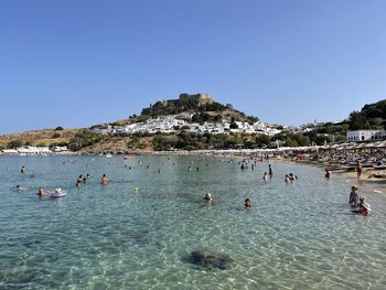 People on beach against clear blue sky