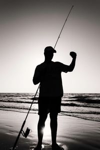Silhouette man fishing on beach against clear sky