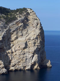 Rock formation by sea against clear sky