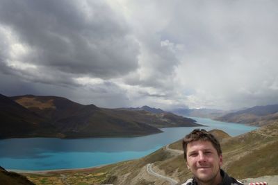 Man on mountain by lake against cloudy sky