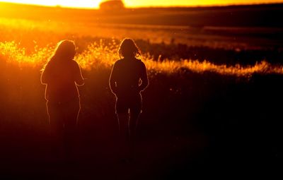 Silhouette women walking on field at sunset
