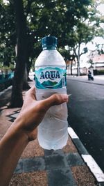 Midsection of man holding bottle against trees in city