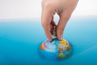 Close-up of human hand holding figurine over globe