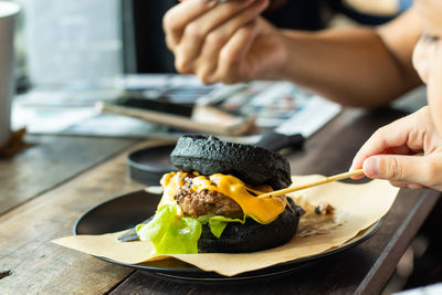 Cropped hands eating hamburger served in plate on table