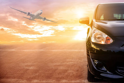 Airplane flying over road against sky during sunset