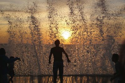 Silhouette man standing at beach against sky during sunset