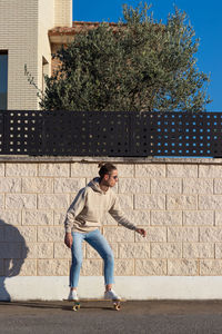 Vertical view of young skater man with bun hairstyle on street against white brick wall 