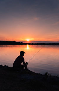 Adolescent boy fishing on shore of lake at sunset in ontario, canada.