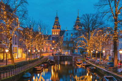 Buildings in city by river against cloudy sky