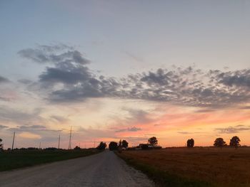 Road amidst field against sky during sunset