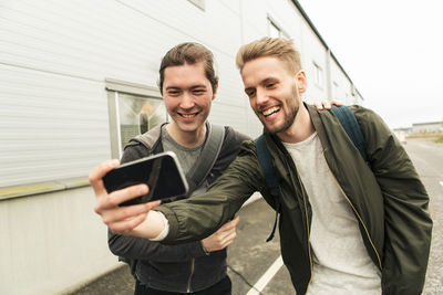 Smiling coworkers taking selfie through mobile phone outside industry