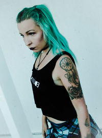 Stylish woman with tattoo standing against white wall