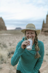 Cheerful female hiker wearing hat while having drink at desert