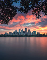 Sea by buildings against sky during sunset