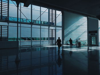 Silhouette people walking in airport seen through glass window