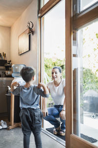 Happy woman looking at son while crouching on doorway