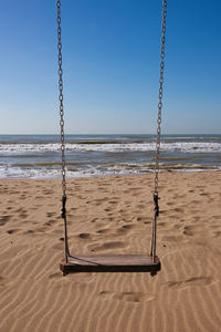 Empty swing on beach against clear blue sky