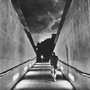 Rear view of men walking on staircase against sky in city