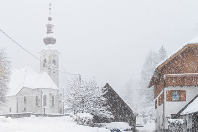 Buildings by snow covered trees against sky