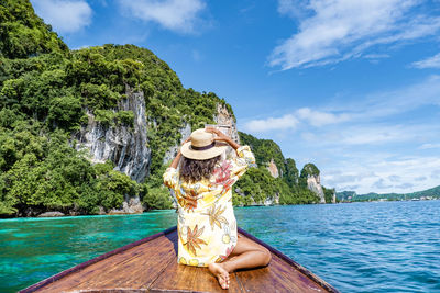 Rear view of woman sitting by sea against sky