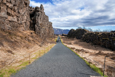 People walking on road by rocky cliffs against sky at thingvellir national park