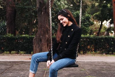 Happy young woman sitting on swing at park