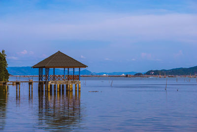 Stilt house by sea against blue sky