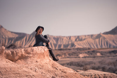 Man sitting on rock against sky