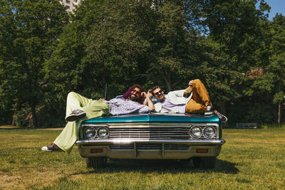 Portrait of happy male friends lying on vintage car in park at sunny day